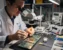 Technician performing BGA rework phone repair course under a microscope on a smartphone logic board at a real repair bench